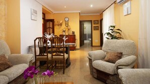 A living room with two sofas, a dining table with chairs, a clock, and a potted plant.