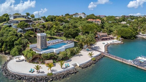 Ovenudblik over et resort med en swimmingpool, en mole og frodig vegetation.
