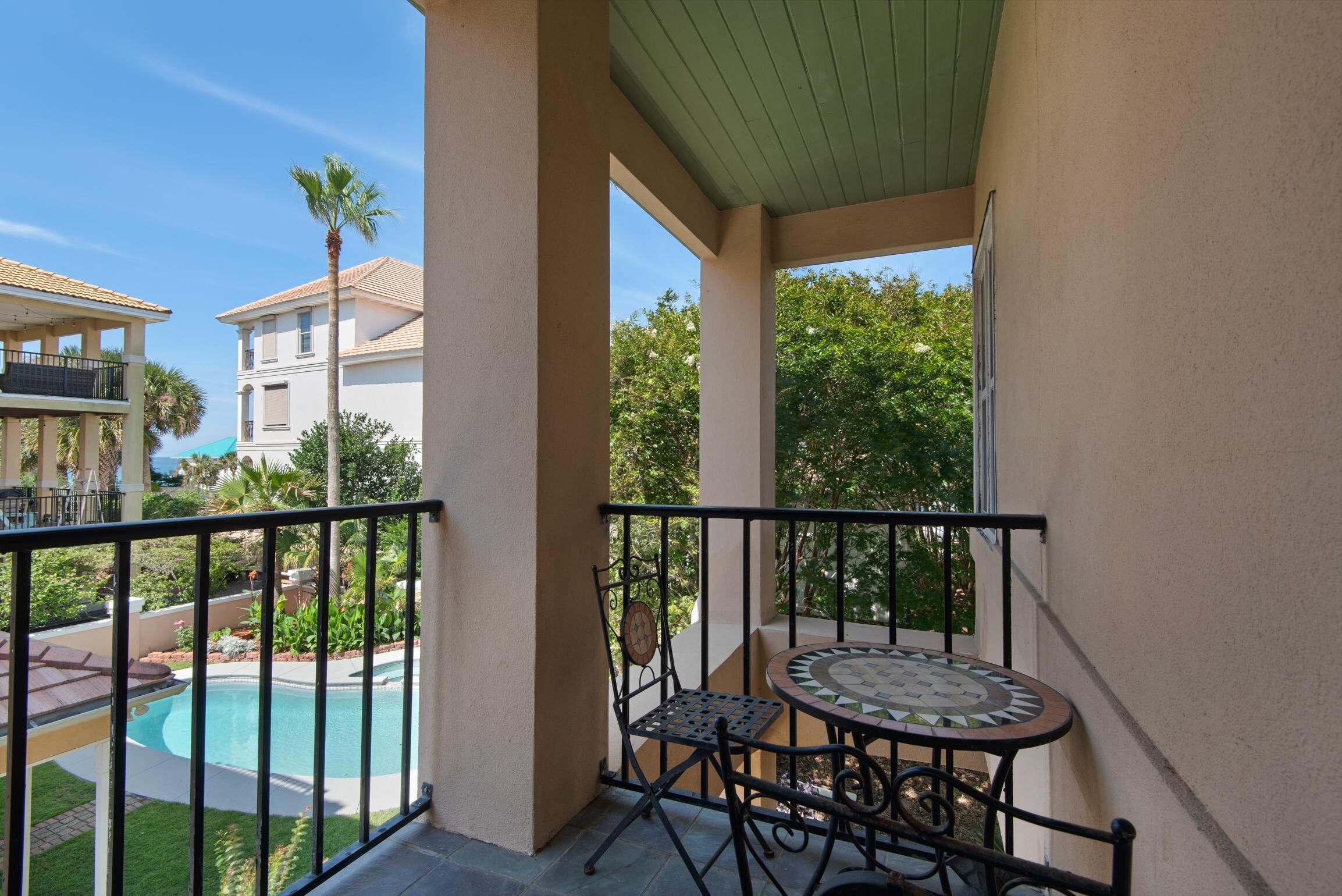 Un balcon avec une table et des chaises, donnant sur une piscine et un espace verdoyant.