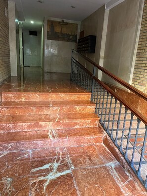 A marble staircase with metal railings leading to a hallway with a cityscape mural on the wall.
