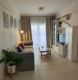 A living room with a sofa, a coffee table, a TV, and a potted plant.