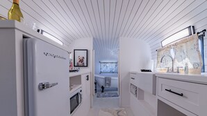 Un pasillo estrecho con armarios blancos, un refrigerador y un cuadro enmarcado a la izquierda.