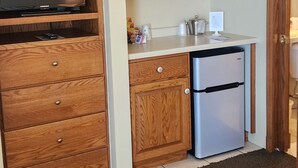 A compact kitchen with wooden cabinets, a built-in TV, a refrigerator, and a countertop with various items. - Snug Harbor Inn - Basic-Water 7 & 10 (Sturgeon Bay)