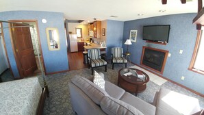 A living room with a sofa, armchairs, a coffee table, a fireplace, and a TV. - Snug Harbor Inn - Studio Suite 201 & 204 (Sturgeon Bay)