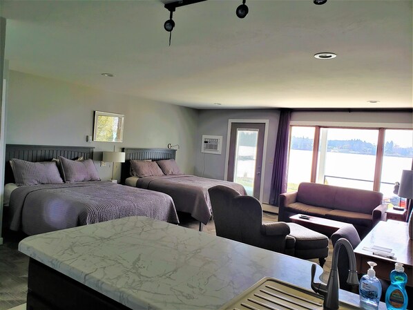 A hotel room with two beds, a sofa, a marble table, and a view of the outdoors. - Snug Harbor Inn - Deluxe 8 & 9 (Sturgeon Bay)