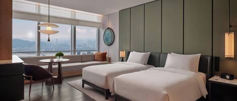 A hotel room with two beds, a sofa, a dining table, and a view of the city.