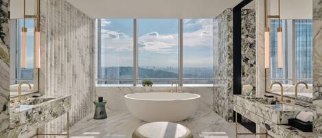 Un bagno moderno con una vasca freestanding, due lavabi e un'ampia finestra con vista sulla città.
