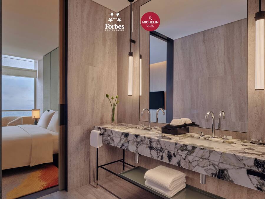 Un baño de hotel moderno con lavamanos de mármol, dos grifos y un espejo grande.