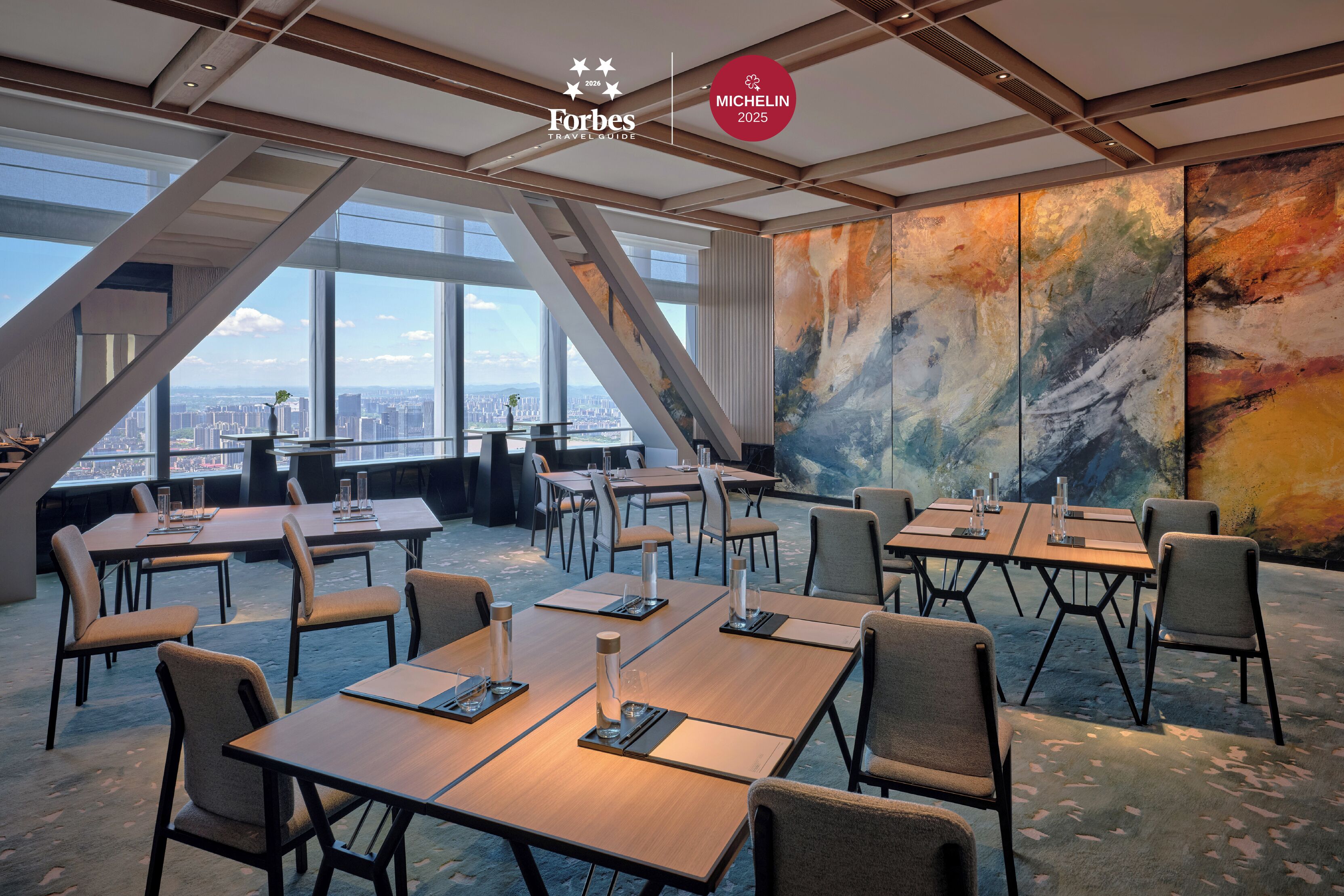 Een moderne hotelvergaderzaal met grote tafels en stoelen, stadszicht door grote ramen en een groot abstract schilderij aan de muur.