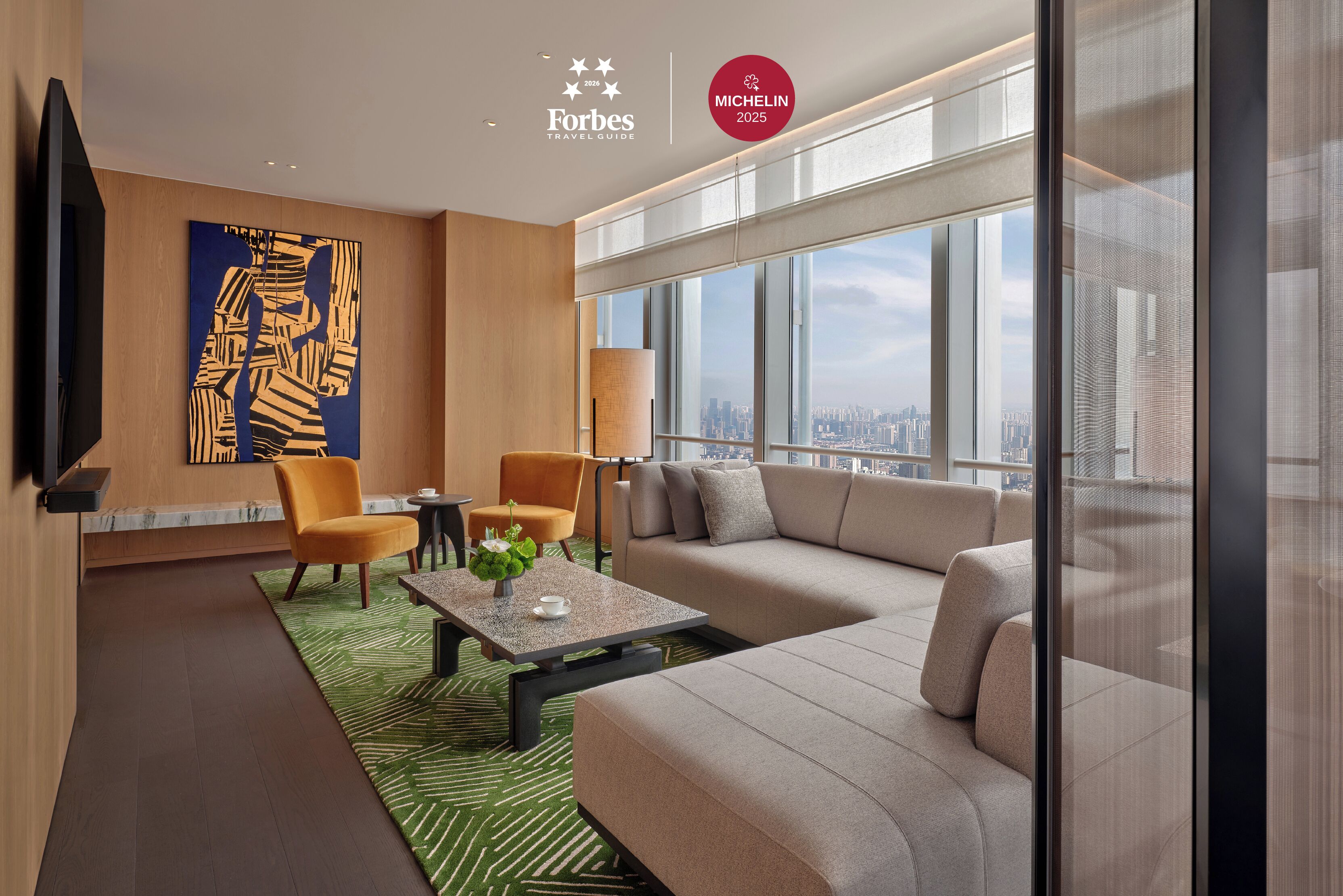 A modern living room with a sofa, chairs, a coffee table, and a large window offering a city view.