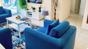 A living room with a blue sofa, white coffee table, and a flat-screen TV. - Beautifully presented 2 bedrooms apartment with a pool and garden view. (Paphos)