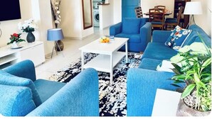 A living room with blue sofas, a white coffee table, and a patterned rug. - Beautifully presented 2 bedrooms apartment with a pool and garden view. (Paphos)