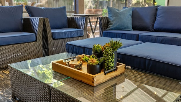 A modern outdoor seating area with wicker furniture, cushions, and a glass coffee table with plants. - Enjoy art and relaxation in this hilltop home (Cedar Key)