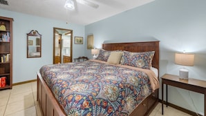 A bedroom with a large bed, a wooden headboard, a nightstand with a lamp, a ceiling fan, a bookshelf, and a mirror. - Enjoy art and relaxation in this hilltop home (Cedar Key)