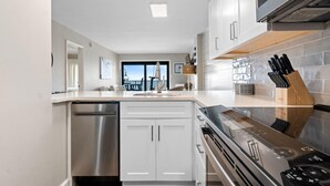 A modern kitchen with white cabinetry, a stainless steel dishwasher, a built-in oven, and a black stove. - Ocean Breeze East 803 (Pensacola)
