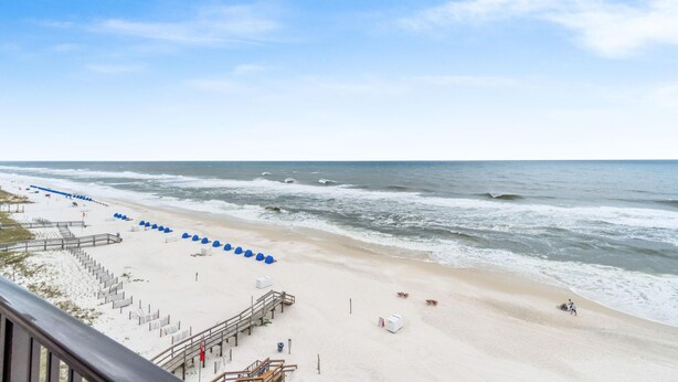 A beach with a wooden walkway and blue umbrellas, leading to the ocean. - Ocean Breeze East 803 (Pensacola)