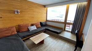 Un soggiorno moderno con una parete in legno, un divano con cuscini, un tavolino da caffè e vista su un paesaggio innevato attraverso ampie finestre.