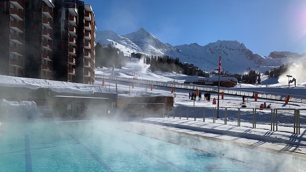 Una piscina con agua cristalina, rodeada de un paisaje nevado y montañas.