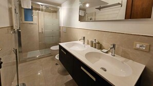 Une salle de bain moderne avec deux lavabos, une douche à l’italienne et un grand miroir.