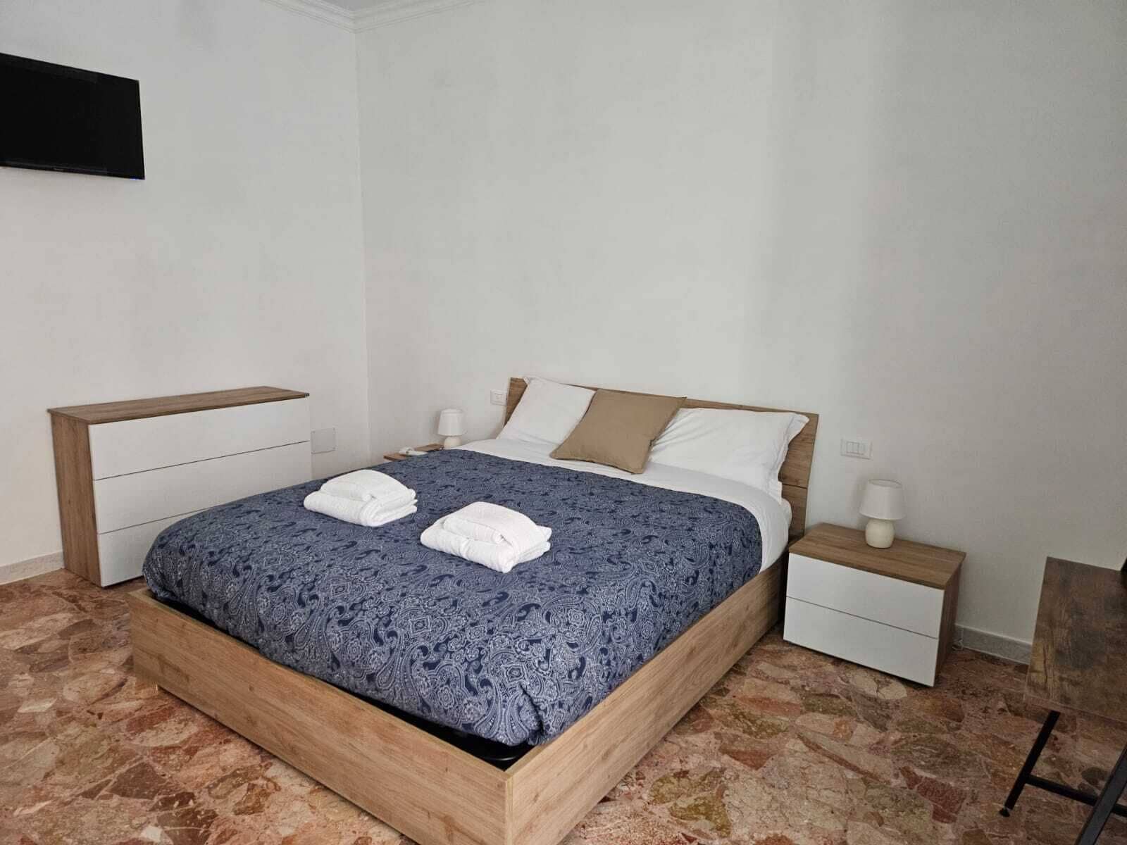 A neatly made bed with a patterned bedspread, two white towels, and a wooden headboard.