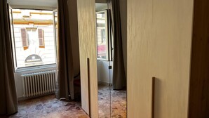Une pièce avec un radiateur, une fenêtre avec des volets et une vue sur un bâtiment à l’extérieur.