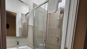 Een moderne badkamer met een douche met glazen wand, een witte wastafel en een spiegel erboven.