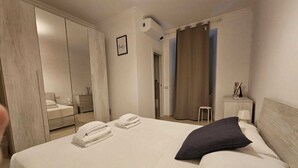 Hotellihuone, jossa on suuri sänky, vaatekaappi, pieni pöytä lampun kanssa ja taulu seinällä.