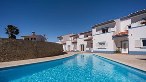 A swimming pool with a stone wall on one side and white buildings with red-tiled roofs in the background. - Vivenda Duneta - in Walking Distance to the Beach by Lisbeyond (Aljezur)
