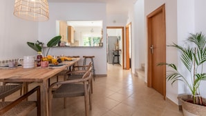 A dining area with a wooden table and chairs, a hanging light fixture, and a view into the kitchen. - Vivenda Duneta - in Walking Distance to the Beach by Lisbeyond (Aljezur)