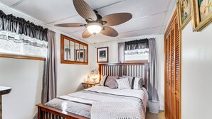 Una camera da letto con un letto, un ventilatore a soffitto, un comodino, uno specchio e una finestra con tende.