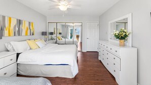 Ein Schlafzimmer mit einem Bett, Nachttischen, einer Kommode, einem Deckenventilator, einem großen Spiegel und Bildern an der Wand.