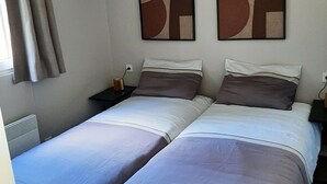 Une chambre avec un lit double, deux lits simples, une table de chevet, une lampe et des œuvres d’art abstraites accrochées au mur.
