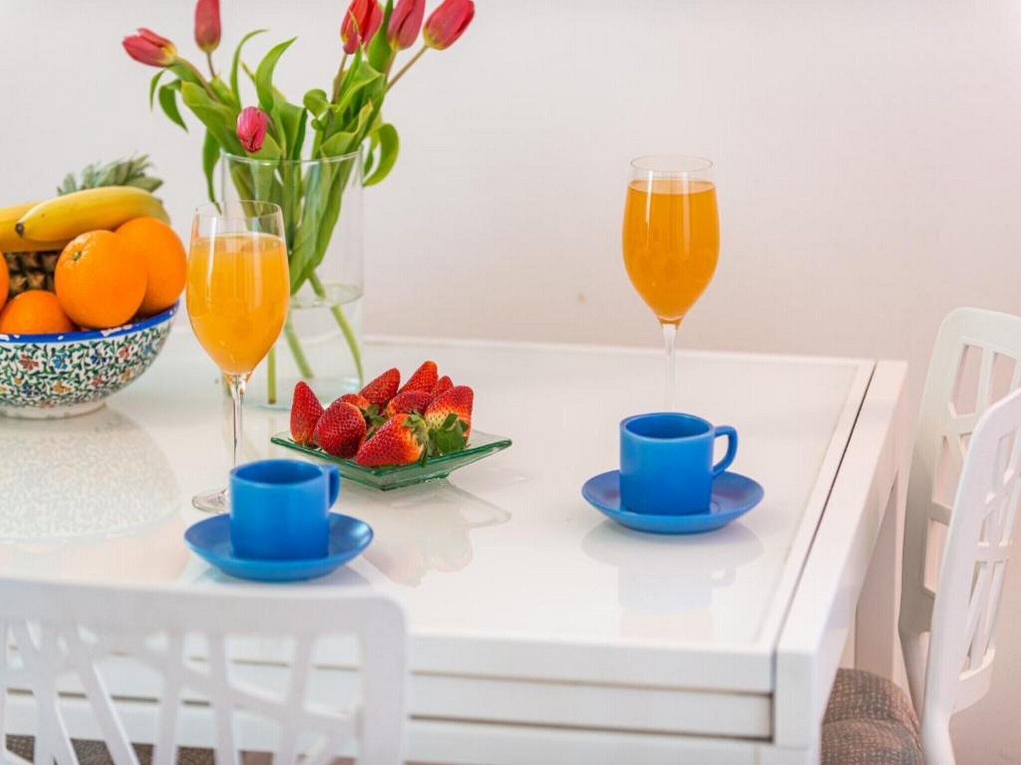 Ett matbord med en skål med frukt, en vas med blommor och två glas apelsinjuice.