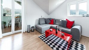 A modern living room with a grey sofa, red and grey cushions, a red coffee table, and a black and white patterned rug.