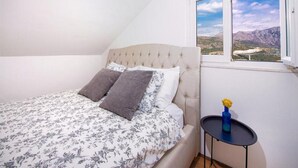 A bedroom with a bed, a window with a mountain view, and a small table with a vase.