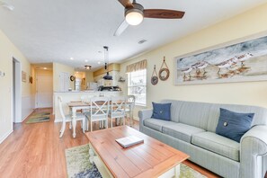 A living room with a gray sofa, a wooden coffee table, and a dining area with white chairs and a table.