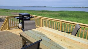 Une terrasse en bois avec un barbecue et des chaises, donnant sur une étendue d’eau.