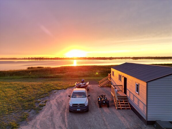 A cabin with a dirt driveway, a parked car, and an ATV. - 6 Mile Lodge (Devils Lake)