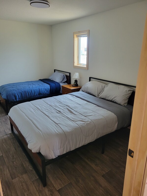 Een slaapkamer met twee bedden, een nachtkastje, een raam en een plafondlamp.