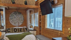 A cozy cabin-style room with a bed, a bench, a television, and a large window. - Blue Lakes Village (Upper Lake)