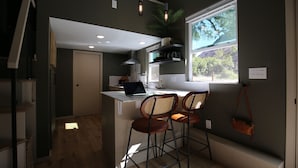 A modern kitchen with a laptop on the island, two bar stools, a window with a view, and a hanging plant. - Blue Lakes Village (Upper Lake)
