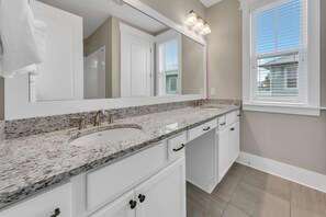 Bathroom features two sinks with gold faucets, a large mirror, and white cabinets.