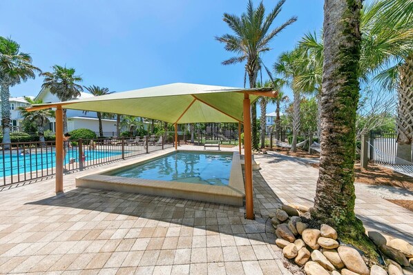 Relax by the pool surrounded by lush greenery and a shaded canopy.