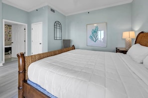 A bedroom with a large bed, a chair, a lamp, and a framed artwork on the wall.