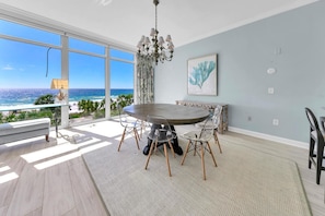 A dining area with a round table, clear chairs, and a view of the ocean.