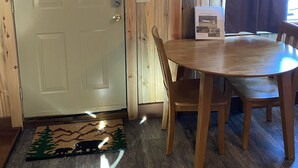 A wooden interior with a white door, a round wooden table with chairs, a coat rack, and a window with curtains. - Bunkhouse at Coal Creek Mountain Lodge (Darby)
