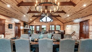 L’intérieur d’un chalet en bois comprend un coin repas avec une grande table dressée pour six personnes, des chaises rembourrées et un lustre.