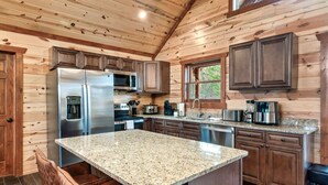 Une cuisine moderne avec un lambris en bois, des comptoirs en granit, des appareils électroménagers en acier inoxydable et un îlot central doté de sièges.