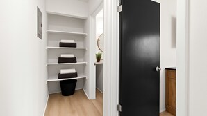 Un couloir étroit aux murs blancs, une porte noire et une étagère intégrée agrémentée de coussins noirs et blancs.