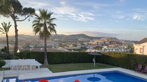 Una piscina con vista sulla città, immersa nel verde e palme.